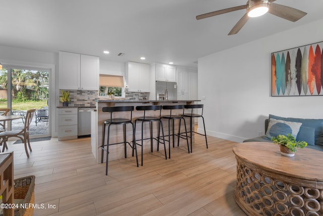 kitchen featuring backsplash, stainless steel appliances, white cabinetry, a breakfast bar area, and ceiling fan