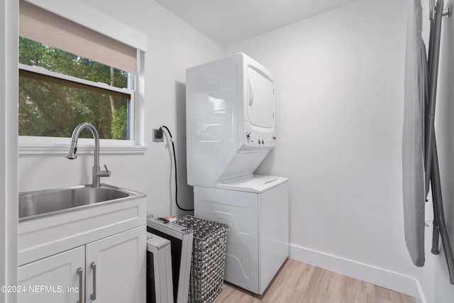 laundry room with sink, stacked washer / drying machine, cabinets, and light wood-type flooring