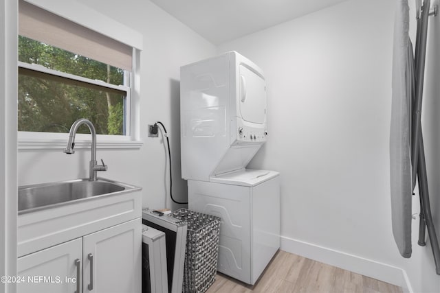 laundry area with baseboards, stacked washing maching and dryer, cabinet space, a sink, and light wood-style floors