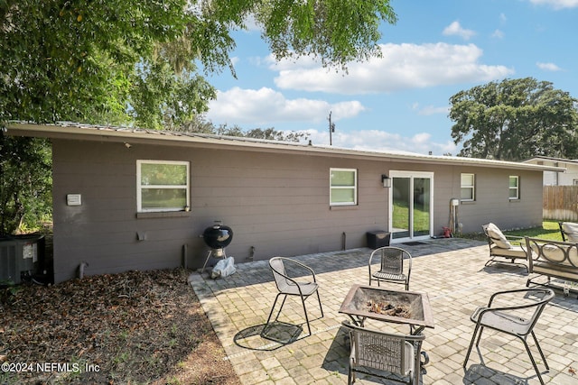 rear view of house with central air condition unit, fence, a fire pit, metal roof, and a patio area