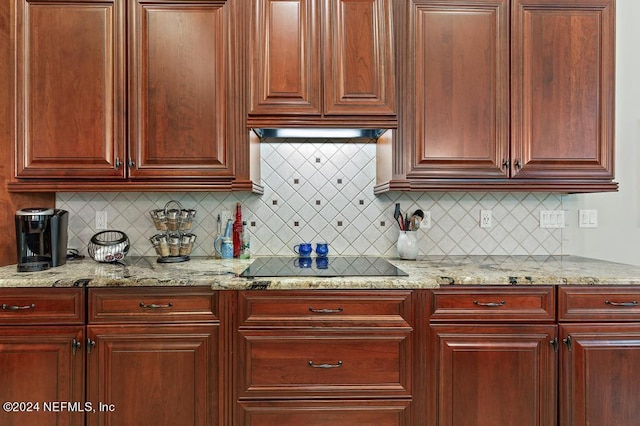 kitchen with under cabinet range hood, light stone counters, black electric cooktop, and reddish brown cabinets