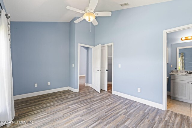 unfurnished bedroom featuring hardwood / wood-style floors, a closet, connected bathroom, high vaulted ceiling, and ceiling fan