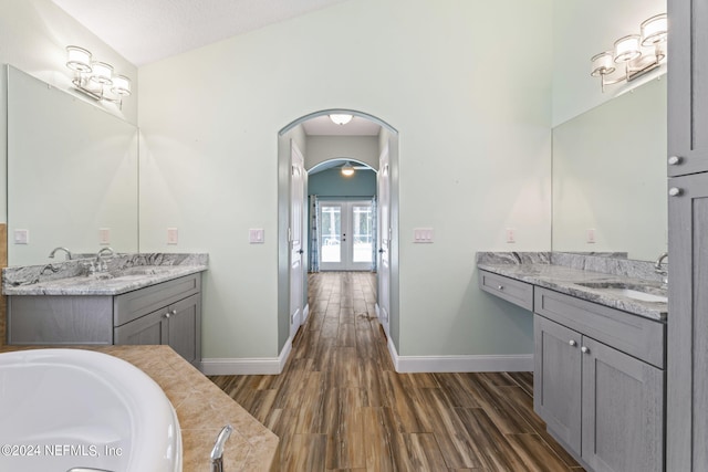 bathroom with a textured ceiling, vanity, a tub to relax in, french doors, and lofted ceiling