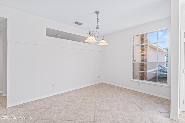 empty room with light tile patterned floors and a notable chandelier