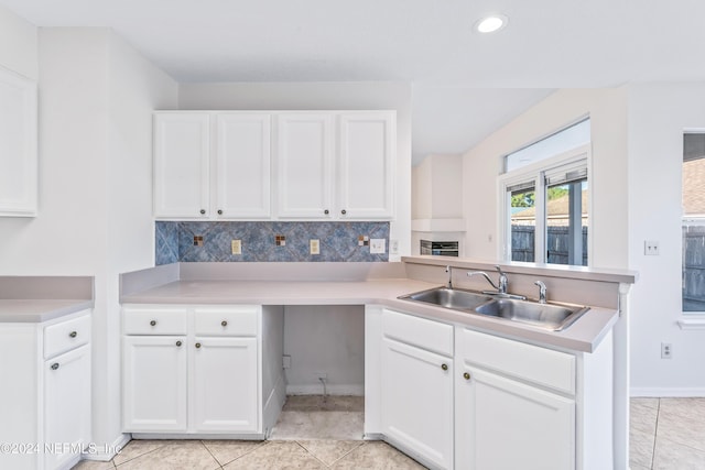 kitchen with sink, light tile patterned floors, kitchen peninsula, decorative backsplash, and white cabinets