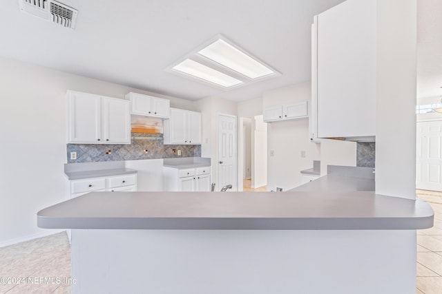 kitchen with tasteful backsplash, kitchen peninsula, white cabinets, and light tile patterned flooring