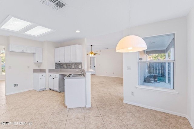 kitchen featuring pendant lighting, kitchen peninsula, ceiling fan, tasteful backsplash, and white cabinetry