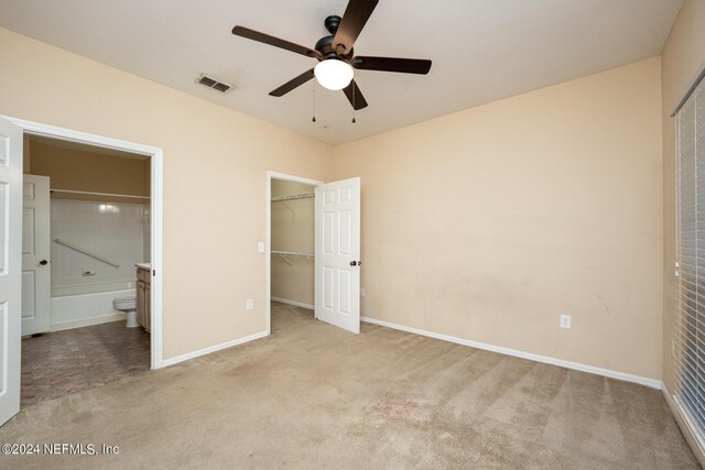 unfurnished bedroom with light colored carpet, a spacious closet, a closet, ceiling fan, and connected bathroom