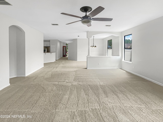 unfurnished living room featuring light carpet, ceiling fan, visible vents, and arched walkways