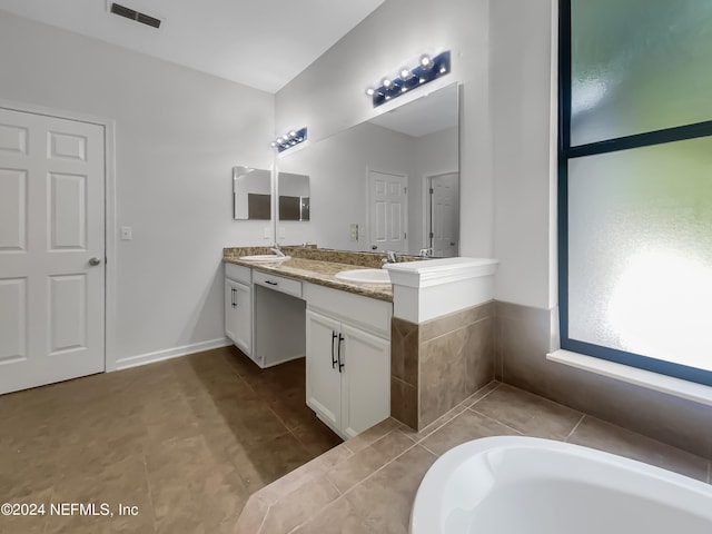 bathroom featuring a washtub, a sink, visible vents, baseboards, and double vanity