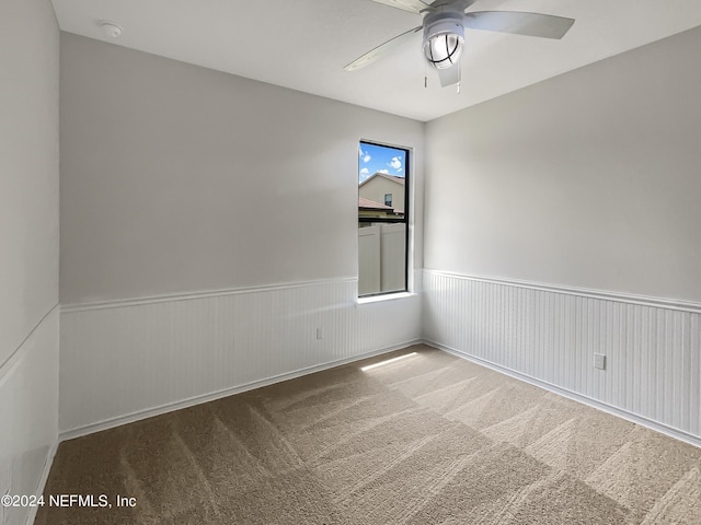 carpeted empty room with ceiling fan and wainscoting