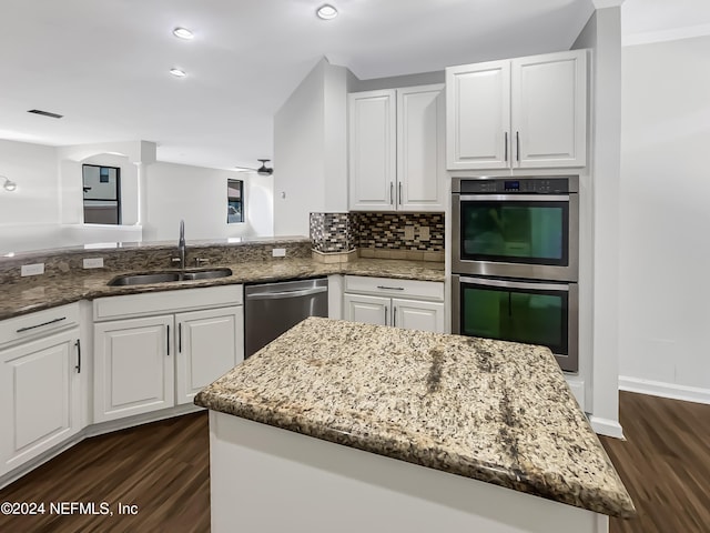 kitchen featuring stone countertops, a center island, stainless steel appliances, white cabinetry, and a sink