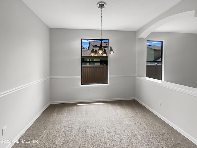 carpeted empty room featuring arched walkways and baseboards