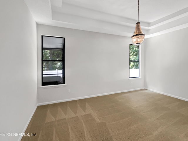 carpeted empty room featuring an inviting chandelier, baseboards, and a tray ceiling