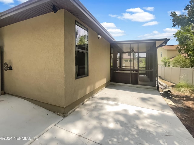 view of property exterior featuring ceiling fan, fence, a sunroom, stucco siding, and a patio area