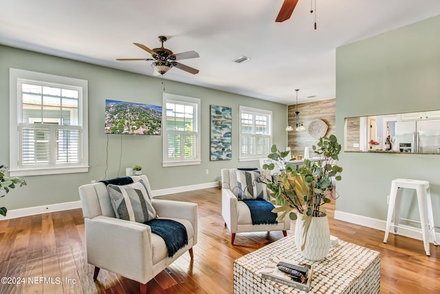 living area with ceiling fan, wood finished floors, visible vents, and baseboards