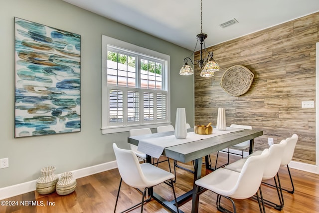 dining area featuring wooden walls, an accent wall, wood finished floors, visible vents, and baseboards