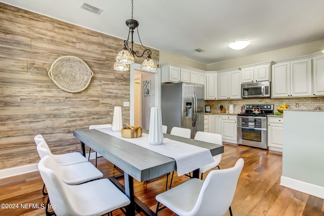 dining area with light wood-style floors, baseboards, visible vents, and wood walls