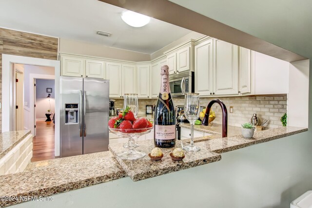 kitchen featuring appliances with stainless steel finishes, wood-type flooring, decorative backsplash, and light stone counters