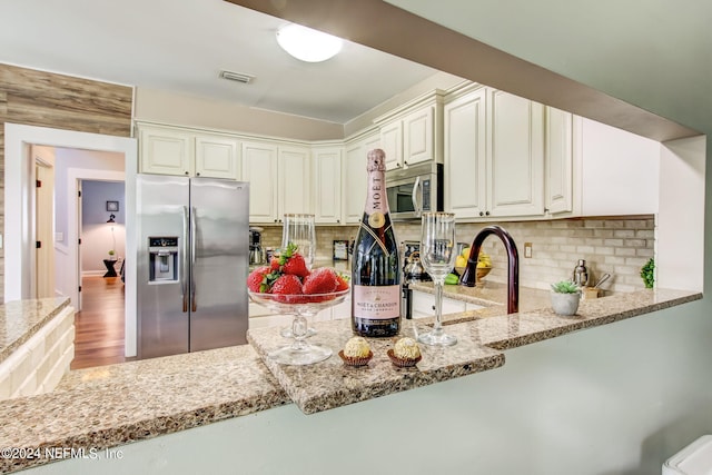 kitchen featuring light stone counters, stainless steel appliances, tasteful backsplash, visible vents, and a sink