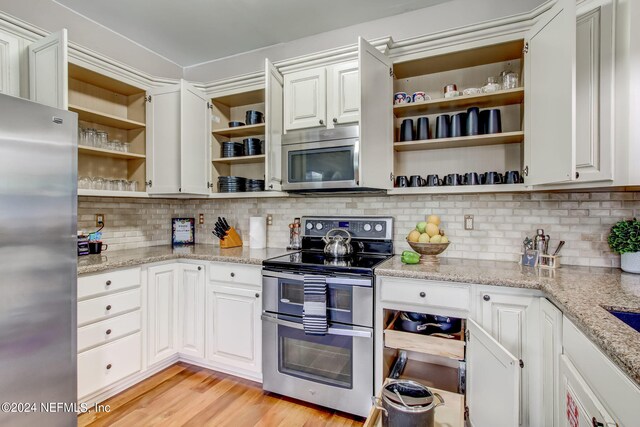 kitchen featuring light wood-type flooring, appliances with stainless steel finishes, decorative backsplash, and white cabinetry