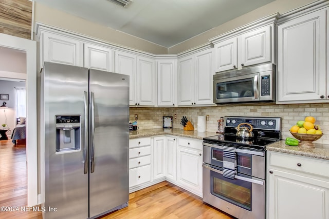 kitchen with light stone counters, stainless steel appliances, decorative backsplash, white cabinets, and light wood-type flooring