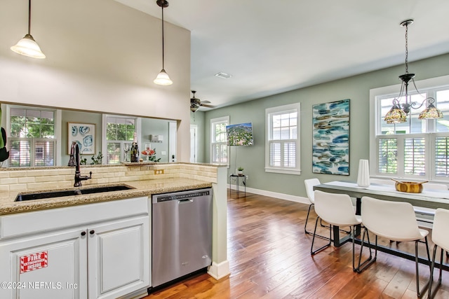 kitchen with a sink, white cabinets, hanging light fixtures, stainless steel dishwasher, and light stone countertops