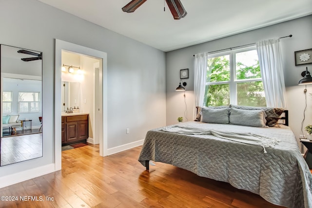 bedroom featuring ensuite bathroom, ceiling fan, a sink, baseboards, and light wood finished floors