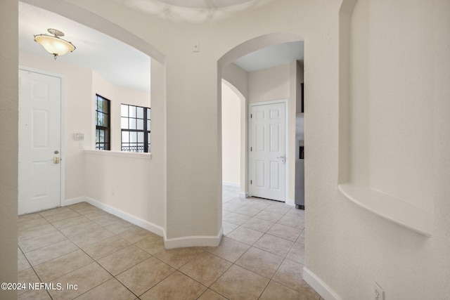 corridor featuring arched walkways, baseboards, and light tile patterned floors