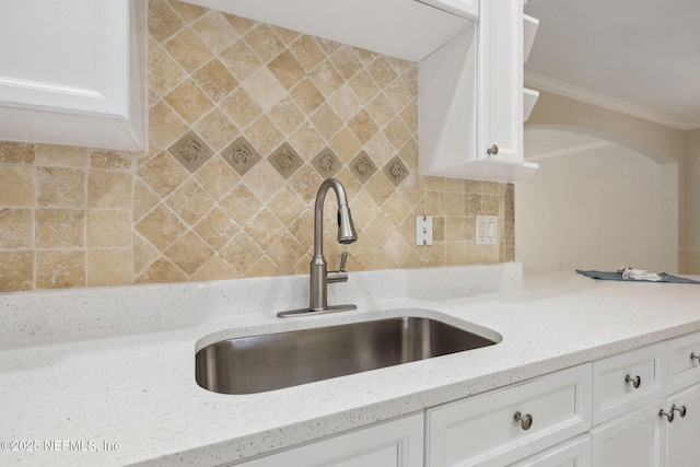 kitchen featuring light stone countertops, white cabinetry, backsplash, and a sink