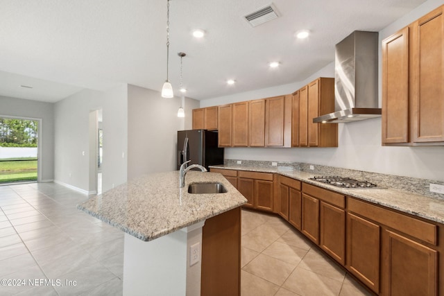 kitchen with a sink, visible vents, black fridge, wall chimney exhaust hood, and a center island with sink