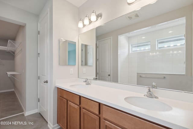 bathroom with double vanity, tile patterned flooring, a spacious closet, and a sink