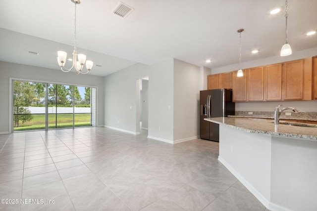 kitchen featuring visible vents, stainless steel fridge with ice dispenser, light stone counters, open floor plan, and a sink