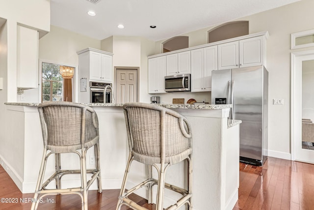 kitchen with hardwood / wood-style floors, appliances with stainless steel finishes, light stone countertops, and white cabinetry