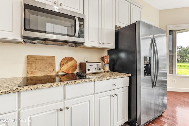 kitchen with light wood-type flooring, appliances with stainless steel finishes, light stone counters, and white cabinetry