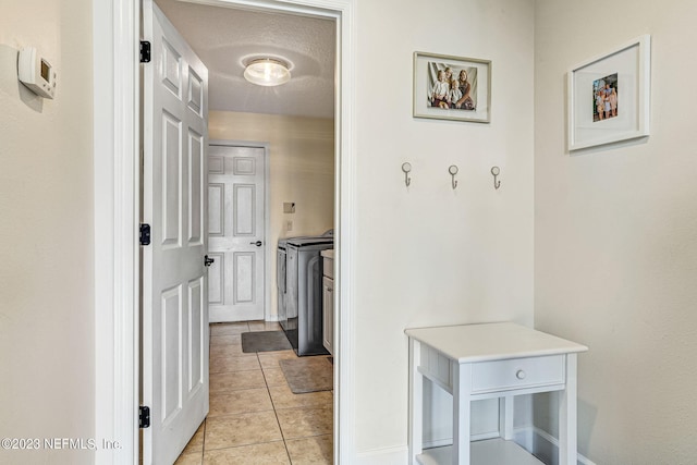 corridor with washer and dryer, a textured ceiling, and light tile patterned flooring