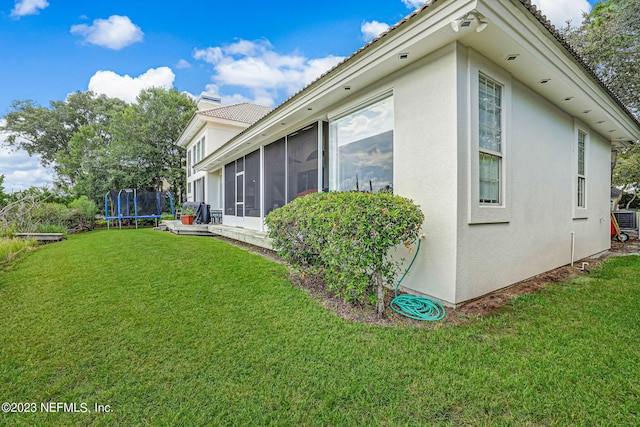 view of property exterior with a lawn, a sunroom, and a trampoline