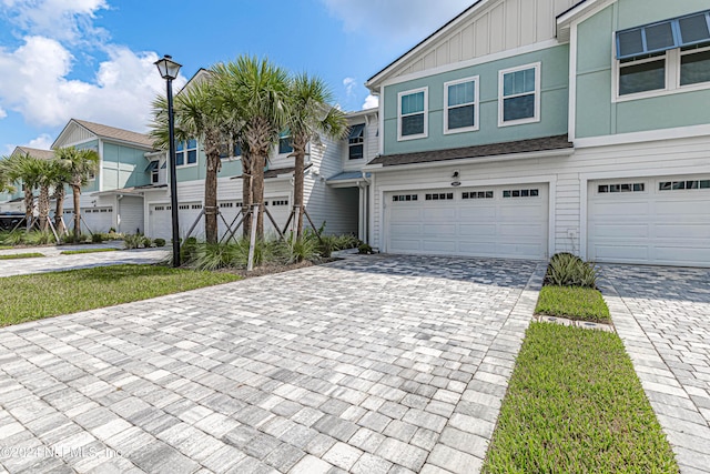 view of property with board and batten siding, decorative driveway, a garage, and a residential view