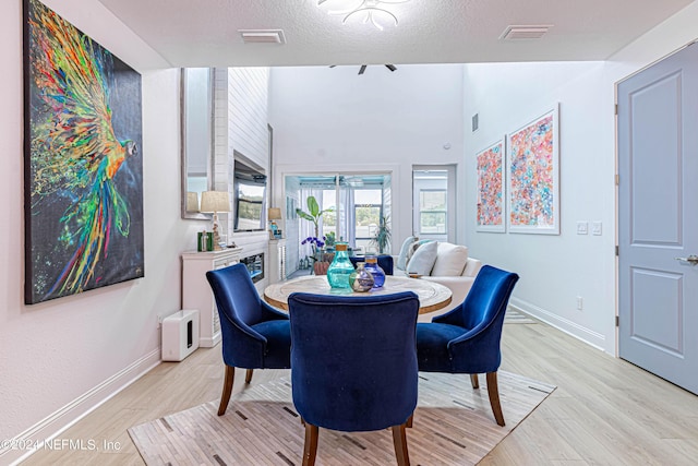 dining room featuring a textured ceiling, baseboards, light wood-style flooring, and visible vents