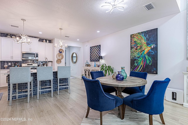 dining room featuring a textured ceiling, visible vents, light wood-type flooring, and a chandelier