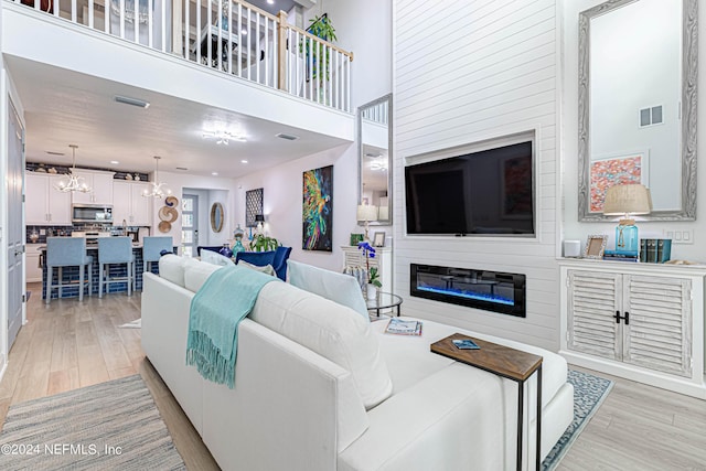 living area featuring an inviting chandelier, a towering ceiling, light wood-style floors, and visible vents