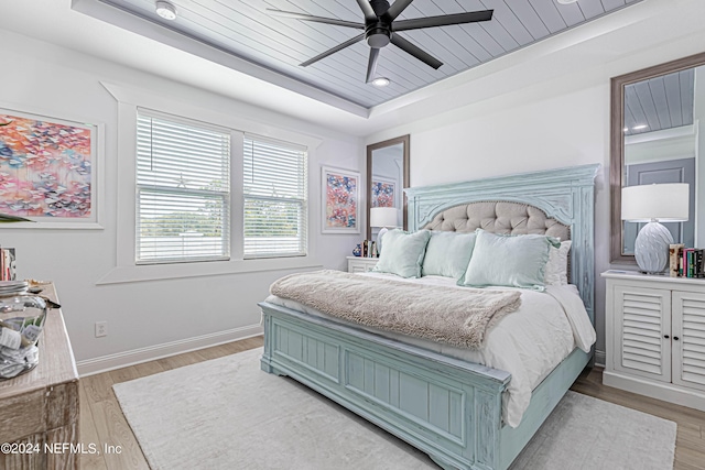 bedroom with a tray ceiling, wooden ceiling, a ceiling fan, baseboards, and light wood-style floors
