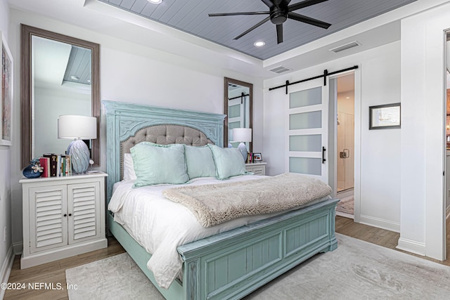 bedroom featuring a tray ceiling, wooden ceiling, a barn door, wood finished floors, and visible vents