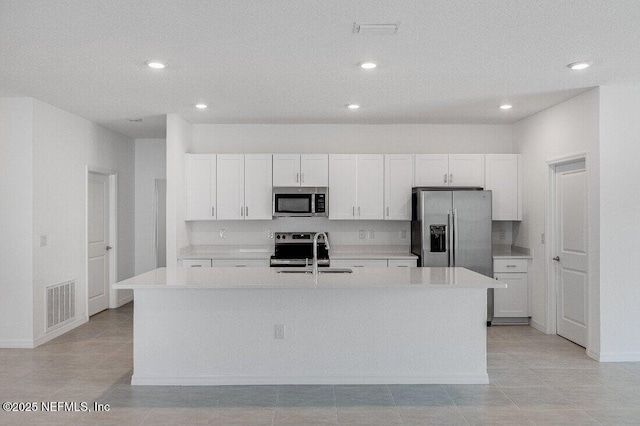 kitchen with light tile patterned flooring, sink, white cabinets, stainless steel appliances, and a center island with sink