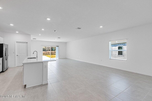 kitchen with stainless steel refrigerator with ice dispenser, white cabinetry, sink, and a kitchen island with sink