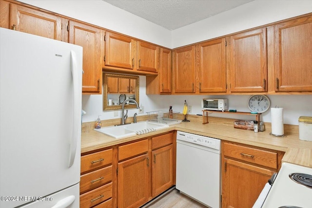 kitchen featuring light countertops, brown cabinetry, a sink, a textured ceiling, and white appliances