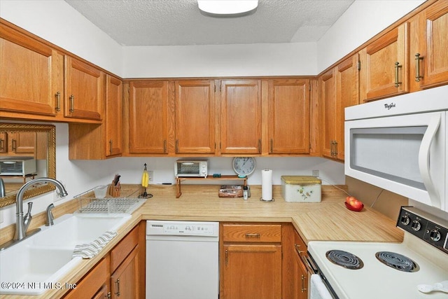 kitchen featuring brown cabinets, light countertops, a sink, a textured ceiling, and white appliances