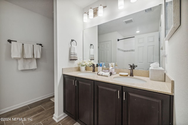 bathroom featuring double vanity, a tile shower, a sink, and wood finish floors