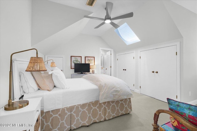 carpeted bedroom featuring two closets, ceiling fan, ensuite bath, and lofted ceiling with skylight