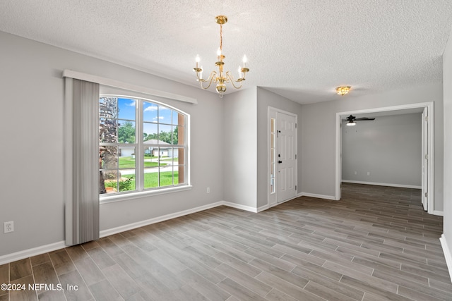 unfurnished room featuring a textured ceiling, wood-type flooring, and ceiling fan with notable chandelier